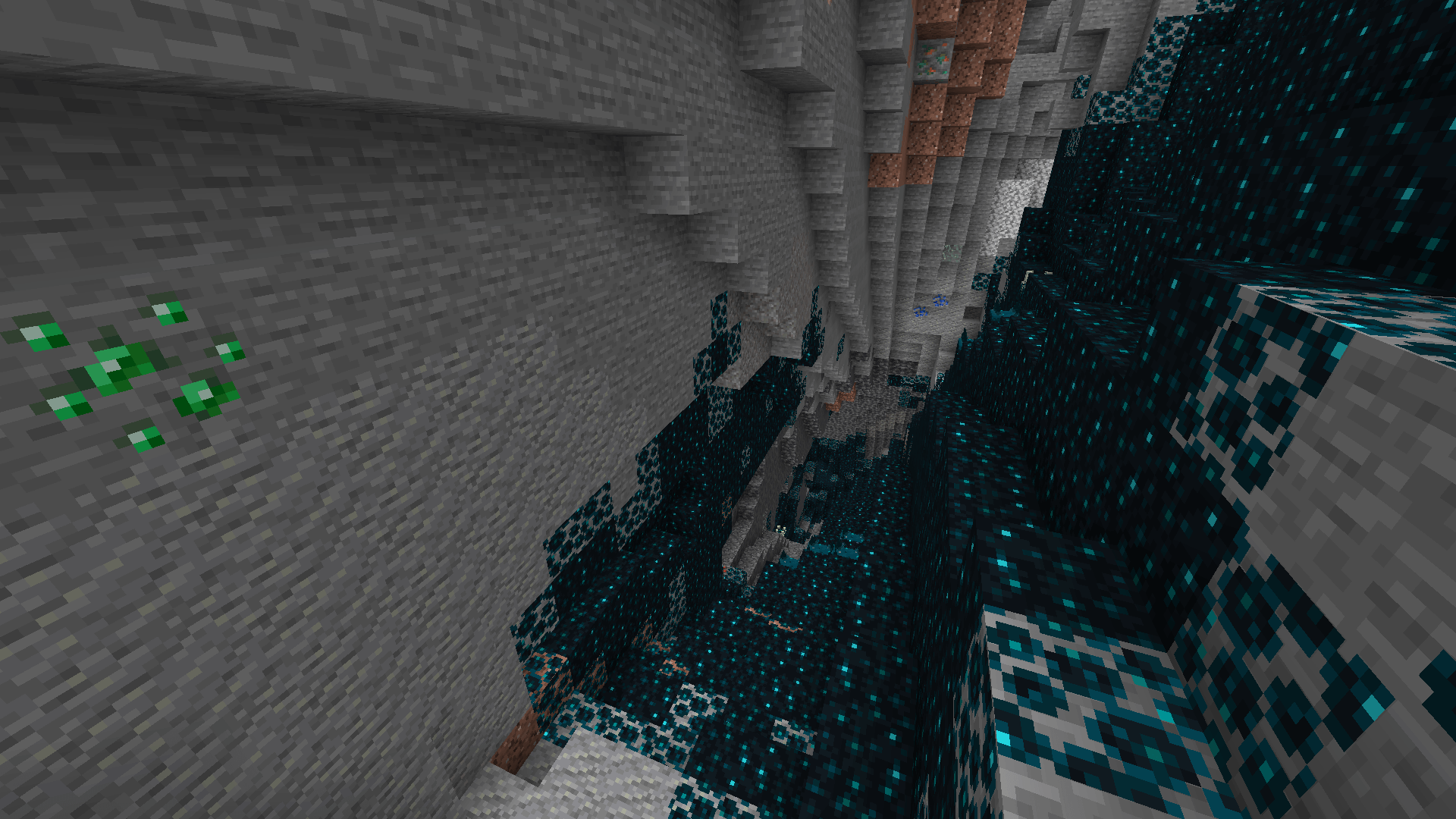 A narrow stone cavern with sculk on the floor. There is an emerald ore on the wall.