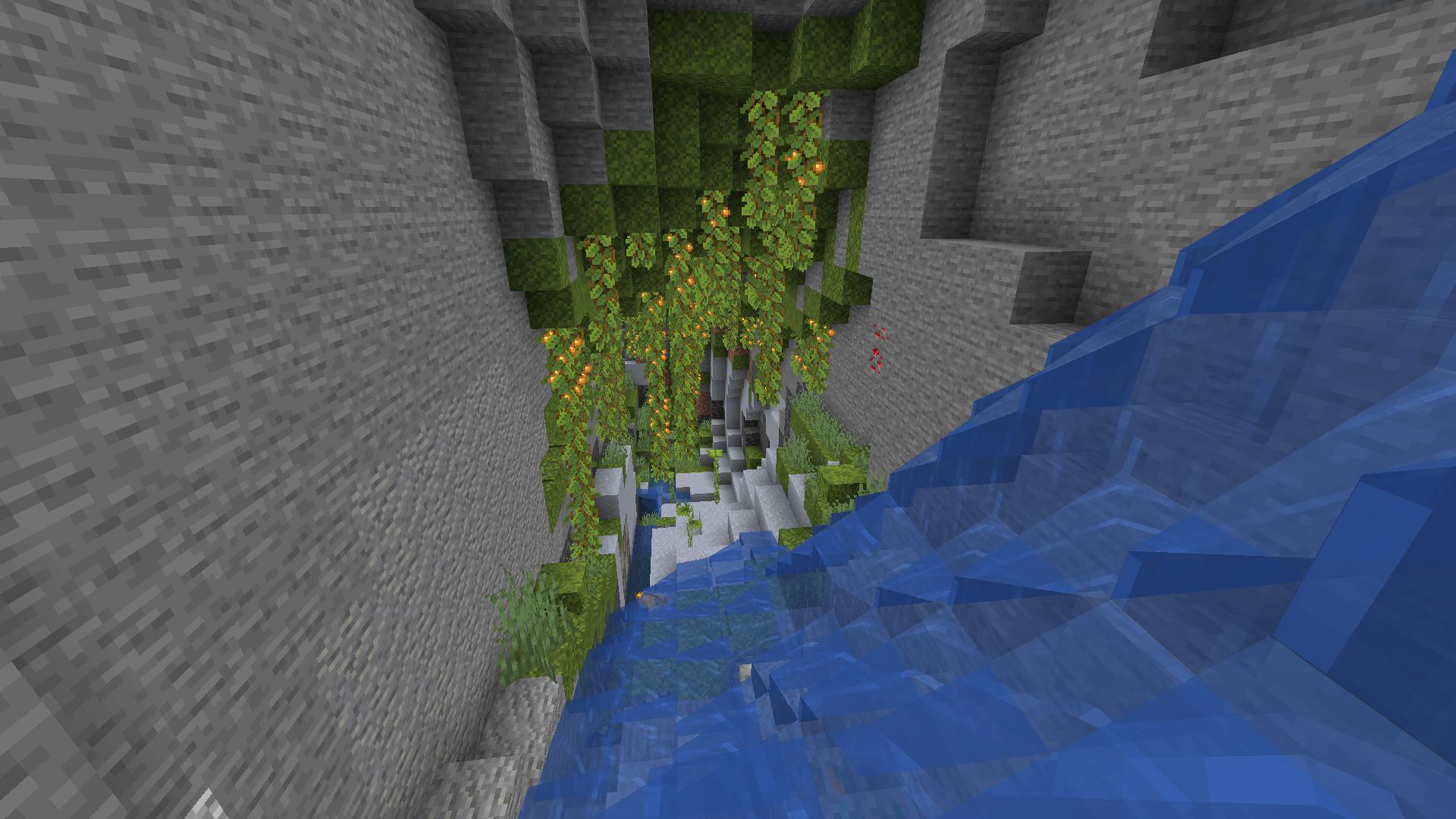 A narrow cave containing the beginning of a lush cave biome. A large cascade of water is flowing in from the near right.