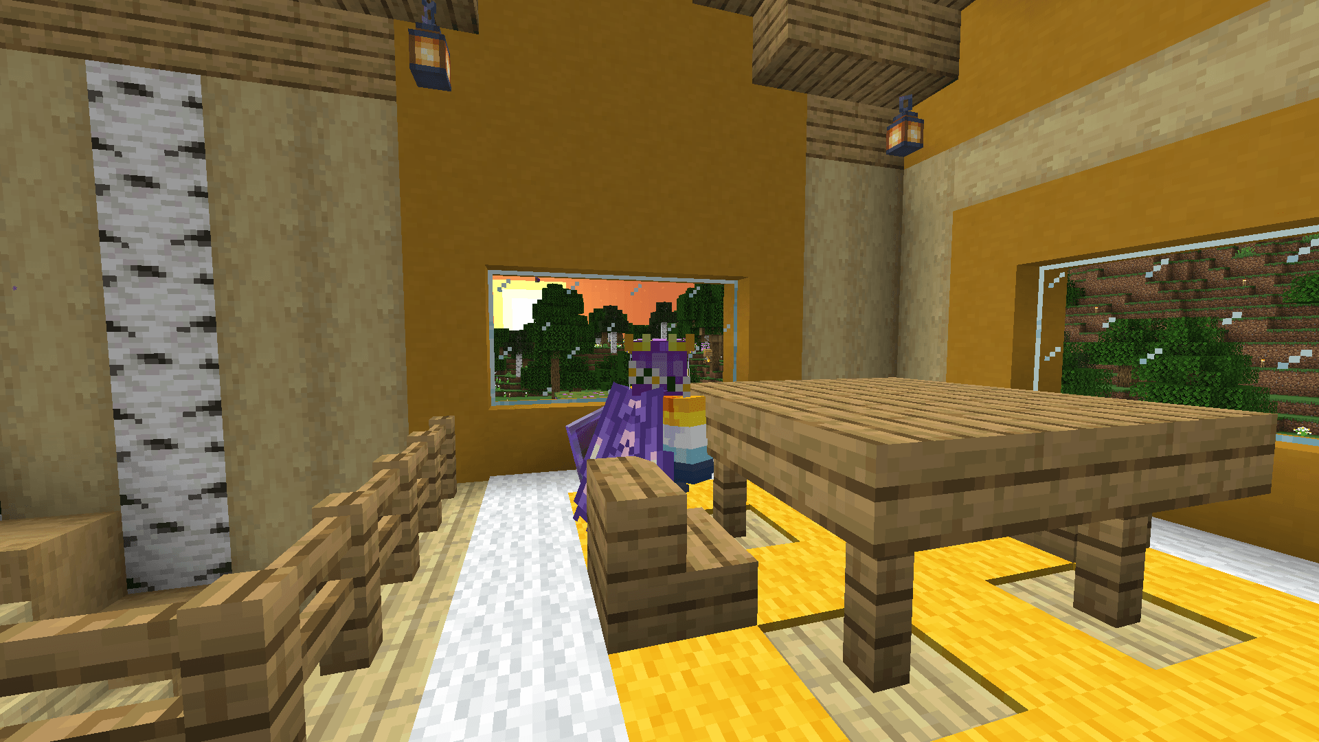 Ela stands at a dining table, looking out the window at the setting sun.